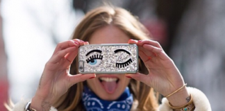 Chica sosteniendo un iPhone a la altura de sus ojos, pues su carcasa tiene un par de ojos pintados.